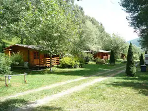 Holzbungalows auf einem Campingplatz im Grünen, mit Rasen, Wegen und Bäumen im Tal.