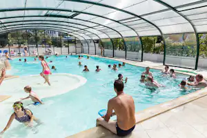 Überdachter Pool im Campingbereich mit vielen Schwimmern, Glaswänden und Liegen am Beckenrand.