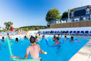 Kinder und Erwachsene im Camping-Pool mit bunten Schwimmnudeln, Liegen am Beckenrand und Gebäude mit Balkon im Hintergrund.