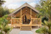 Camping La Vallée des Vignes Lodge-Zelt auf Stelzen mit überdachter Veranda und Sitzmöglichkeiten