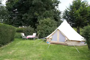 Campingzelt im grünen Garten mit Liegestühlen und Tisch, umgeben von Hecken und Bäumen.