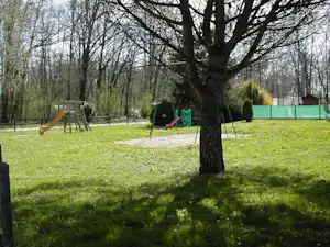 Spielplatz auf dem Campingplatz: Rutsche und Schaukel im grünen Garten mit Rasen, Bäumen und Hecken.