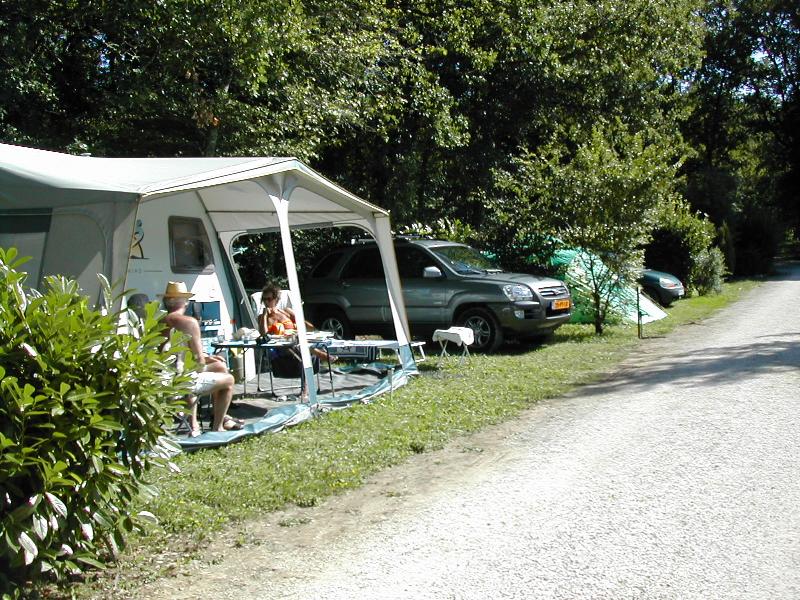 Campingbus mit Vorzelt und Sitzbereich am Stellplatz, daneben mehrere Autos und ein Weg durch grünes Gelände.