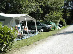 Campingbus mit Vorzelt und Sitzbereich am Stellplatz, daneben mehrere Autos und ein Weg durch grünes Gelände.