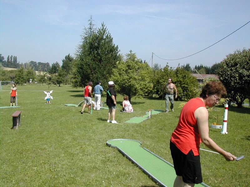 Minigolfanlage auf dem Campingplatz: Spieler stehen auf dem Rasen, ein Mann schiebt den Ball über die Bahn.