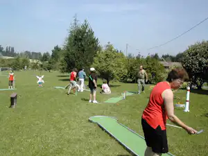 Minigolfanlage auf dem Campingplatz: Spieler stehen auf dem Rasen, ein Mann schiebt den Ball über die Bahn.