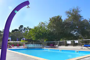 Blaues Camping-Schwimmbecken mit lila Bogen am Rand, Zaun und Liegen im Hintergrund.