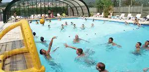 Beheiztes Camping-Poolbecken mit vielen Schwimmern, aufblasbarer gelber Rutsche im Vordergrund und Liegen am Rand.