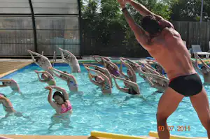 Kinder im Camping-Pool planschen, während ein Erwachsener am Beckenrand steht; Liegen und Sonnenschirme sind zu sehen.