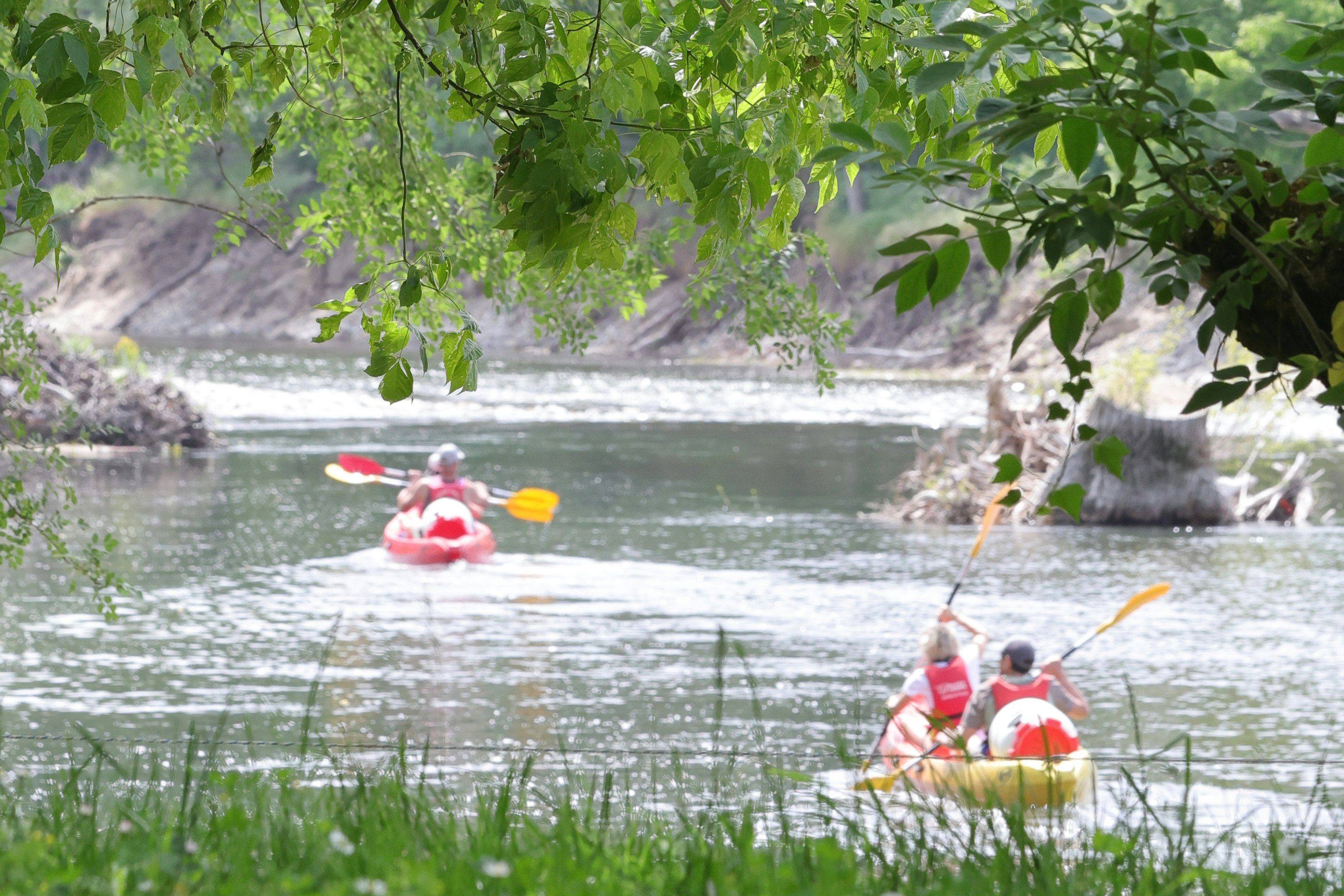 Zwei Schlauchboote mit roten Schwimmwesten auf einem Fluss, umgeben von grünen Bäumen und Ufervegetation.