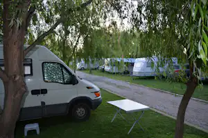 Weißes Wohnmobil am Campingplatz, daneben ein Tisch und Stühle auf dem Stellplatz, im Hintergrund Zelte und Bäume.