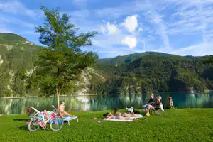 Camping Lago Arsiè - Liegewiese vom Campingplatz mit Liegestühlen in der Sonne und mit Blick auf den See und die Berge