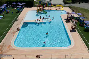 Großes Schwimmbecken mit mehreren Personen, Liegen und Sonnenschirmen auf einer Terrasse, daneben ein Spielbereich im Campingplatz.