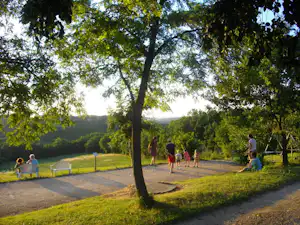 Campingweg zwischen grünen Bäumen, Rasenflächen und einer Hecke, im Hintergrund Wiesen und ein paar Personen.