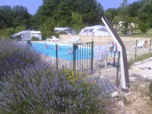 Eingezäunter Pool mit Liegen und Zelt auf dem Campingplatz, im Hintergrund weitere Wohnwagen und Bäume.