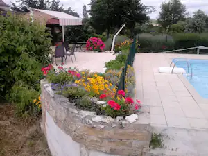 Blumenbeet mit bunten Pflanzen vor einem Pool auf der Terrasse, daneben Gartenwege und ein Pavillon mit Sitzgelegenheiten.