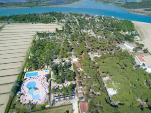 Luftaufnahme eines Campingplatzes am Fluss mit Stellplätzen, Wegen, Bäumen und einem Poolbereich mit Liegen.