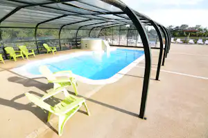 Beheizter Camping-Pool mit Liegen und Sonnenschirmen unter einem Glasdach, im Hintergrund Zaun und Bäume.