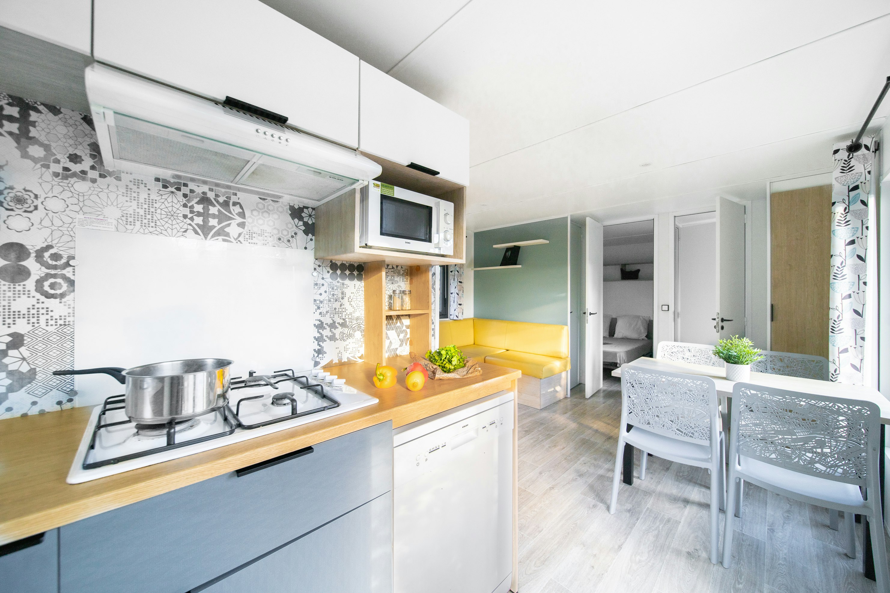 Wohnküche mit Gasherd, Küchenzeile, gelbem Sofa und Esstisch im hellen Mobilhome-Bereich.