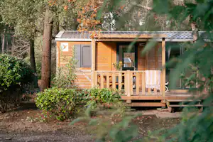 Holzunterkunft mit Terrasse im Wald, mit Markise, Fenster und Sitzbereich auf dem Holzdeck.