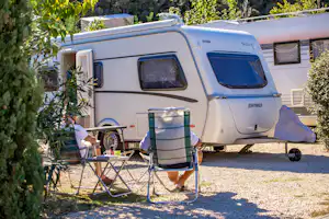 Wohnmobil mit Vorzelt und Campingstühlen am Stellplatz, daneben Tisch und Pflanzen im Grünen.