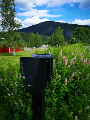 Schwarzer Grill im Garten mit blühenden Sträuchern, Rasen und Blick auf grüne Berge im Hintergrund.