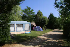 Zelte auf einem Campingplatz: ein Wohnwagen mit Vorzelt und ein weiteres Zelt neben einem Kiesweg.