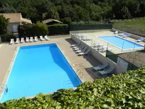 Zwei Camping-Pools auf einer Terrasse mit Liegestühlen, Glasgeländer und Hecken vor einem Gebäude.