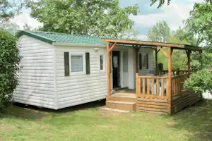 Weiße Unterkunft mit Holzveranda und Treppe, umgeben von Rasen und Bäumen im Campingbereich.
