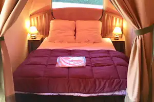 Campingbett mit zwei Kissen, warmen Nachttischlampen und Holzverkleidung im Zelt, Blick auf Decke und Vorhänge.