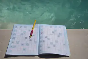 Offenes Wochenplan-Buch mit Stift auf einer Bank, im Hintergrund ein grünes Wasserbecken.