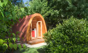 Orangefarbenes Zelt mit Holzveranda am Campingplatz, umgeben von dichtem Grün und Bäumen im Hintergrund.