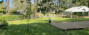 Campingwiese mit Zelt und Pavillon zwischen Bäumen, gepflasterter Weg und Rasenfläche im Hintergrund.