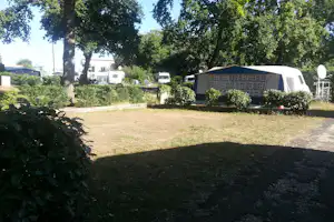 Campingzelt mit gemusterten Wänden auf einem Stellplatz, umgeben von Büschen, Bäumen und einem Wohnwagen im Hintergrund.