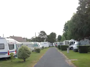 Campingplatz-Gasse mit Wohnmobilen und Caravans, Rasenflächen und Hecken, links und rechts geparkte Fahrzeuge.
