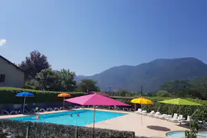 Campingpool mit bunten Sonnenschirmen, Liegen und Blick auf grüne Berge und Hügel im Hintergrund.
