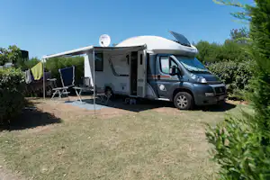 Wohnmobil mit Markise, Vorzelt und Tisch am Stellplatz, daneben Wäscheleine und Campingstühle im Grünen.