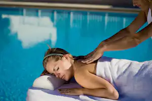 Frau liegt am Pool auf Handtüchern, während eine zweite Person eine Massage am Rücken gibt.