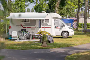 Wohnmobil auf einem Campingplatz mit Vorzelt, Stühlen und Tisch, daneben ein Sonnenschirm im Schatten der Bäume.
