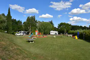Wohnmobil-Stellplatz mit Spielplatz, Rasenfläche, Picknicktisch und Bäumen, im Hintergrund weitere Fahrzeuge und Wohnwagen.