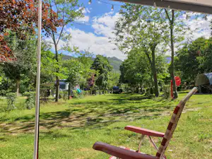 Campingplatz mit Rasenfläche, Sitzbank und Bäumen, im Hintergrund Zelte und ein Weg zwischen den Stellplätzen.