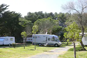 Wohnmobil auf dem Campingplatz im Grünen, neben einem weiteren Fahrzeug, mit Bäumen und Rasenfläche im Hintergrund.