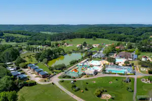 Luftaufnahme eines Campingplatzes mit Schwimmbecken, Spielbereich und See, umgeben von Wiesen, Bäumen und mehreren Gebäuden.