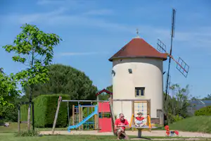 Wasserturm am Campingplatz mit Spielplatz, Rutsche und Schaukel, daneben Rasen und Hecken.