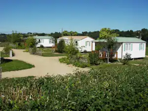 Mehrere Mobilheime auf einem Campingplatz, mit Kieswegen, kleinen Bäumen und grünem Garten im Vordergrund.