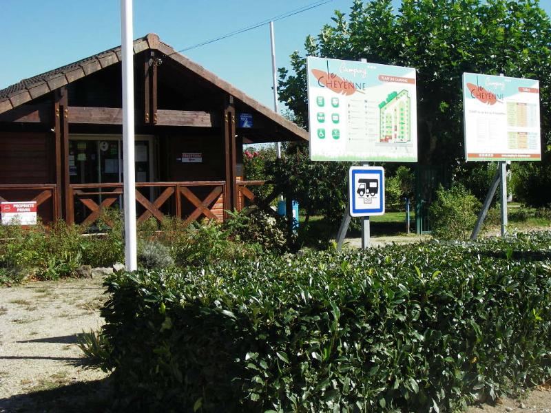 Holzhütten am Campingplatz mit Wegweisern und Schildern, Hecken und Kiesweg vor den Gebäuden.