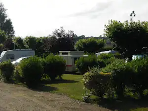 Wohnwagen und ein Mobilheim auf einem Campingplatz, umgeben von Hecken und Rasenfläche.
