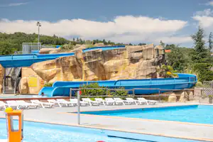 Blaue Wasserrutsche an einer Felswand, daneben Pool und weiße Liegestühle auf der Terrasse.