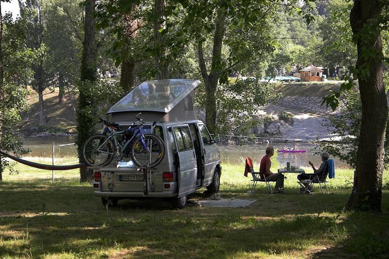 Camping Le Clapas - Campingbulli zwischen Bäumen mit davor sitzenden Campern