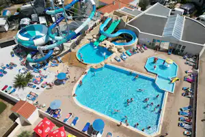 Großer Camping-Pool mit Sonnenliegen, daneben ein Kinderbecken und blaue Wasserrutschen auf dem Gelände.